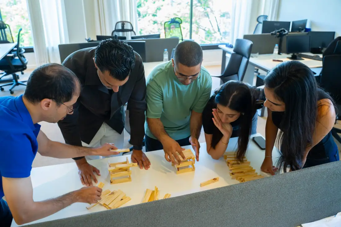 Cinq participants penchés sur une construction en tasseaux de bois posée sur une table.